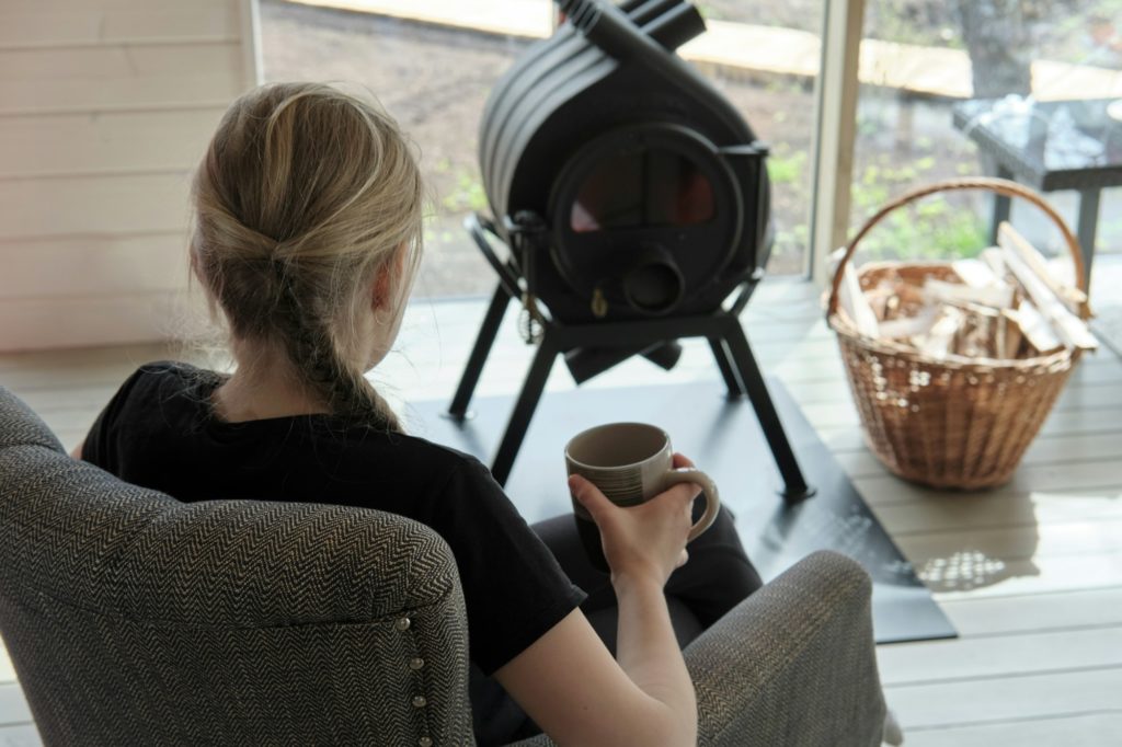 Rear view of teenage girl resting near the heating stove with mug of tea.