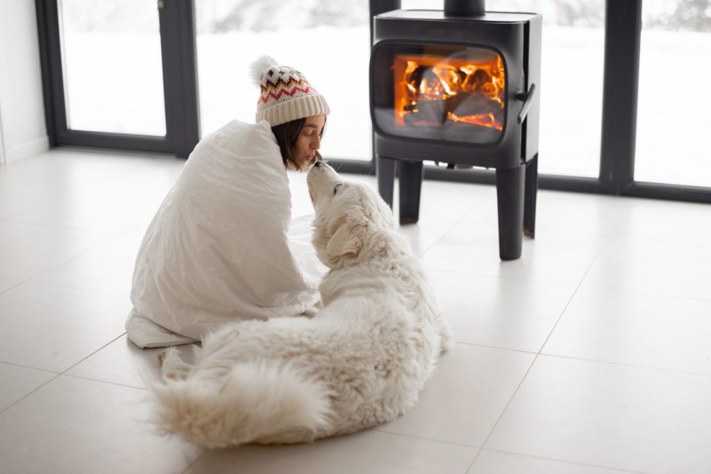 Woman with dog at home with burning fireplace during wintertime